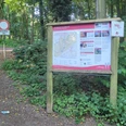 Infotafel am Wanderparkplatz im Wald, daneben breiter Forstweg und Verkehrsschild