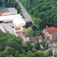 Luftaufnahme einer Brauerei mit Hallen, Schornstein und Parkplatz am Waldrand