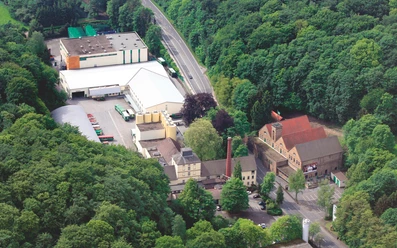 Luftaufnahme Brauerei Luftaufnahme einer Brauerei mit Hallen, Schornstein und Parkplatz am Waldrand
