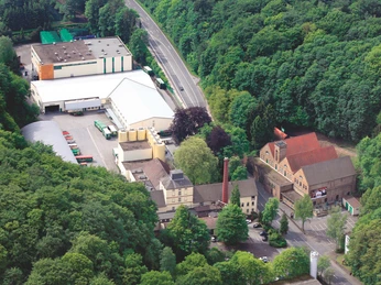 Luftaufnahme Brauerei Luftaufnahme einer Brauerei mit Hallen, Schornstein und Parkplatz am Waldrand
