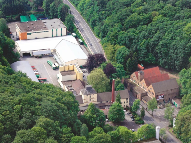 Luftaufnahme Brauerei Luftaufnahme einer Brauerei mit Hallen, Schornstein und Parkplatz am Waldrand