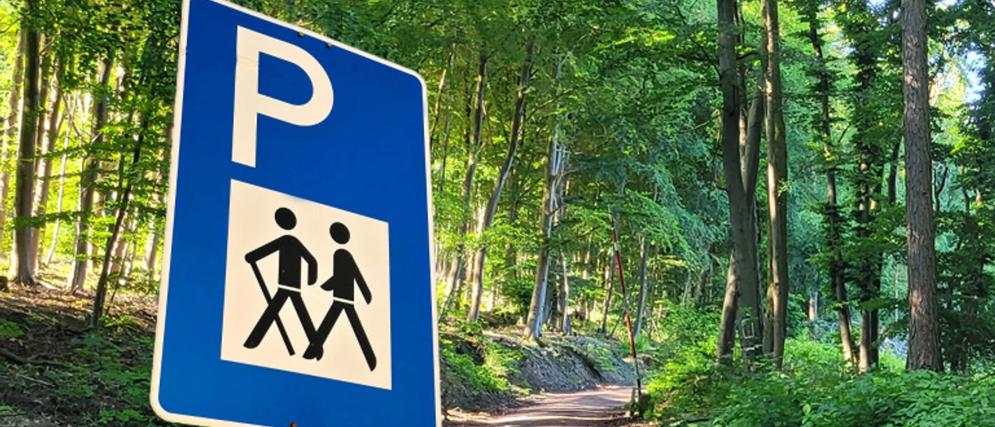 Parkplatzschild mit Wanderpiktogramm an Waldweg im Grünen