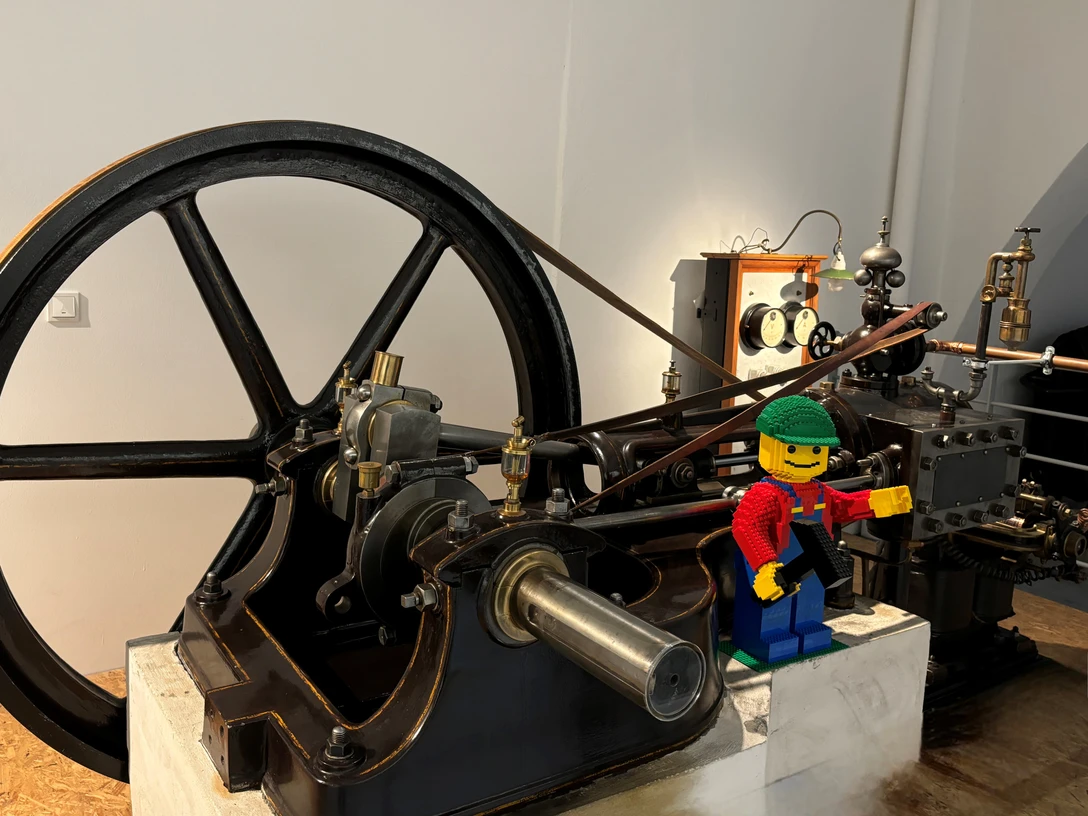 Lego-Tag Lego-Arbeiterfigur mit Werkzeug steht an einer historischen Industriemaschine.