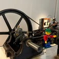 Lego-Tag Lego-Arbeiterfigur mit Werkzeug steht an einer historischen Industriemaschine.