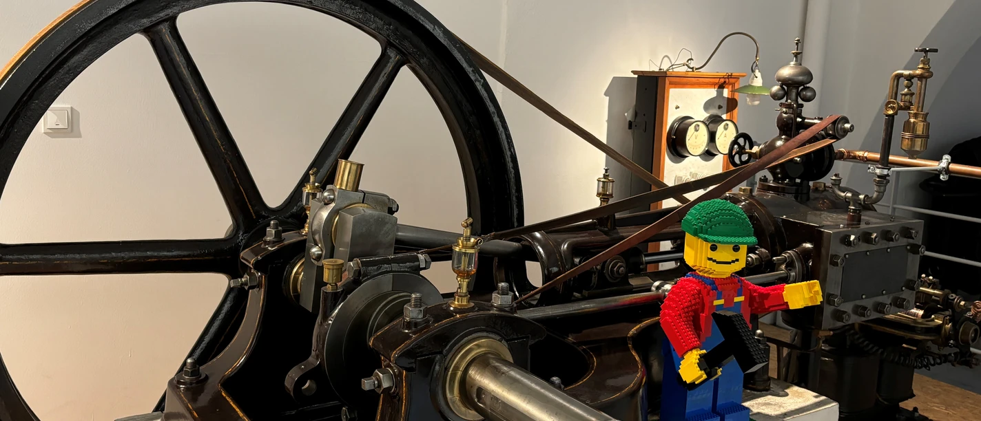 Lego-Tag Lego-Arbeiterfigur mit Werkzeug steht an einer historischen Industriemaschine.