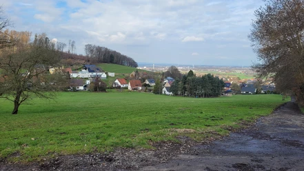 Wiehengebirge Blick über grüne Wiese auf Häuser am Hang und weite Landschaft unter wolkigem Himmel