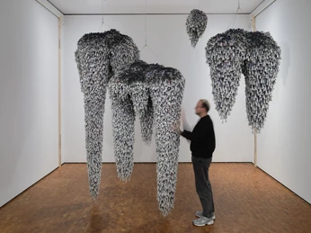 Installation view HERE AND NOW at the Museum Ludwig. De/Collecting Memories Museum Ludwig, Cologne 2026 Hanging sculptural forms made up of many small elements with a blurred person in the room.