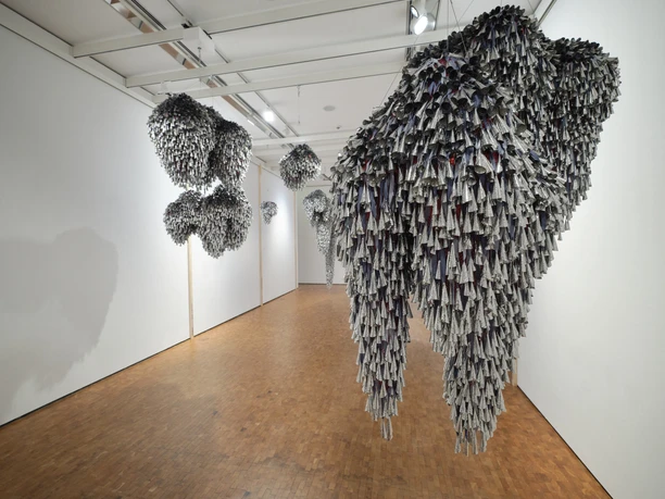 Installationsansicht HIER UND JETZT im Museum Ludwig. De/Collecting Memories Museum Ludwig, Köln 2026 Hängende Skulpturen aus dicht gefalteten Papierformen in einem weißen Galerieraum.