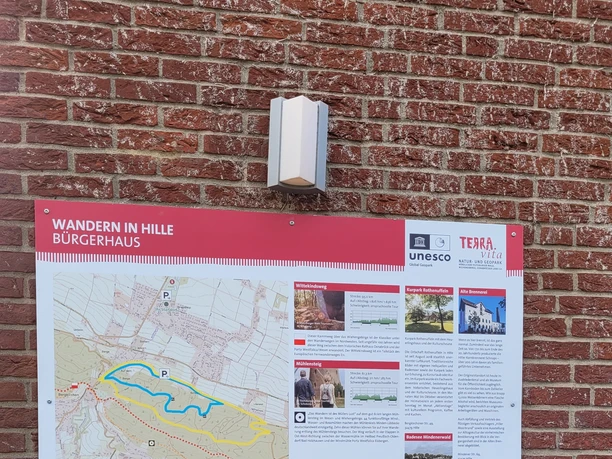 Infotafel „Wandern in Hille“ am Bürgerhaus mit Routenkarte an roter Backsteinwand
