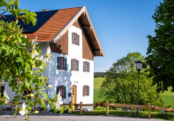 Pilgerhaus Wildsteig Weißes Landhaus mit rotem Dach vor grünen Wiesen und Bäumen an einem sonnigen Tag