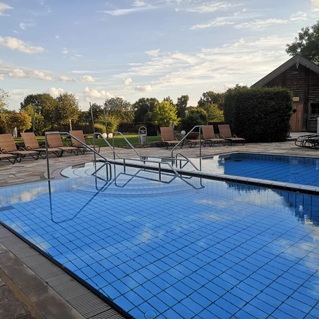 Aussenpool.jpg Außenpool im BadeLand mit blauen Fliesen, Liegen und Holzhaus im Hintergrund.