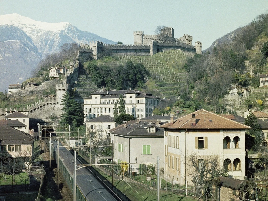 Bellinzona: hinten die Montebello-Burg, vorne der Personenzug | Bellinzone: à l’arrière-plan, le château de Montebello; au premier, le train de voyageurs | Bellinzona: dietro il Castello di Montebello, davanti il treno passeggeri, ≈ 1975.