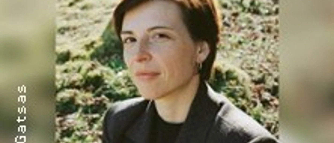 Porträt einer kurzhaarigen Person im dunklen Mantel vor grasbewachsener Landschaft