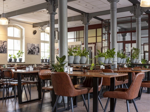 Alte Feuerwache Heller Innenraum mit braunen Sitzmöbeln, Pflanzen auf Tischen und hohen Stützen aus Stahl
