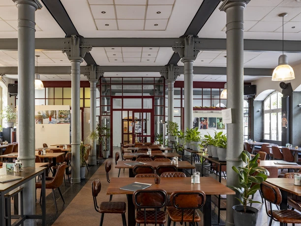 Alte Feuerwache Bright dining room with high pillars, large windows, wooden tables and lots of plants