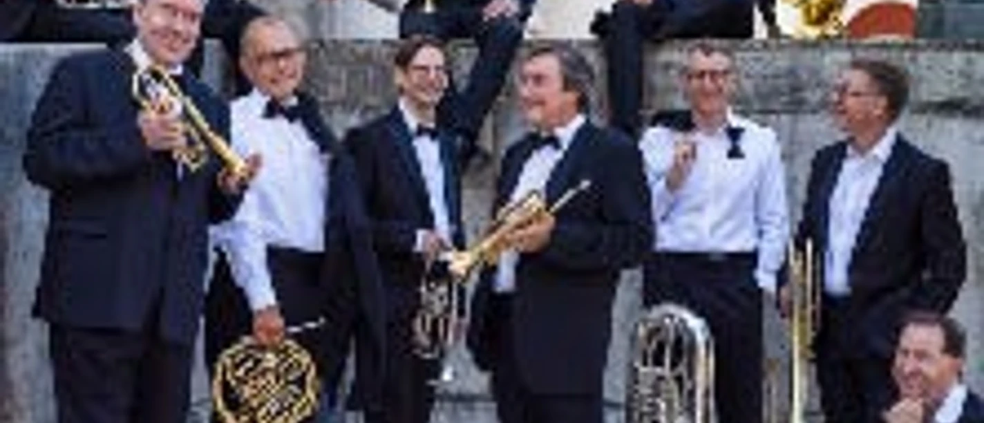 Eine Gruppe festlich gekleideter Musiker mit Blechblasinstrumenten vor steinernem Gebäude