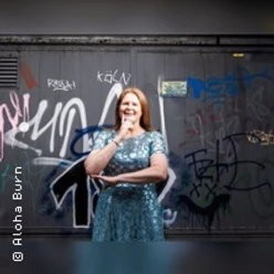 Frau im glitzernden Kleid steht vor einer mit Graffiti bedeckten Wand und lächelt.