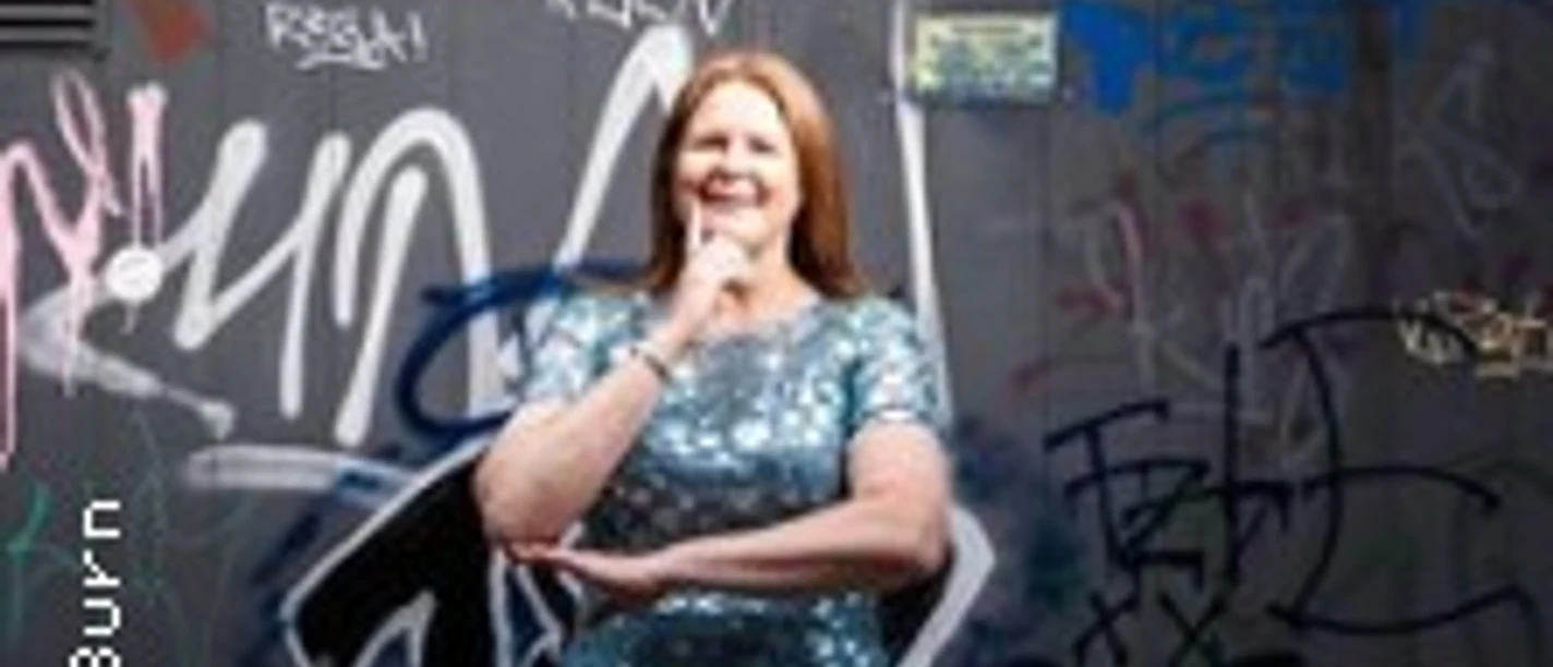 Frau im glitzernden Kleid steht vor einer mit Graffiti bedeckten Wand und lächelt.