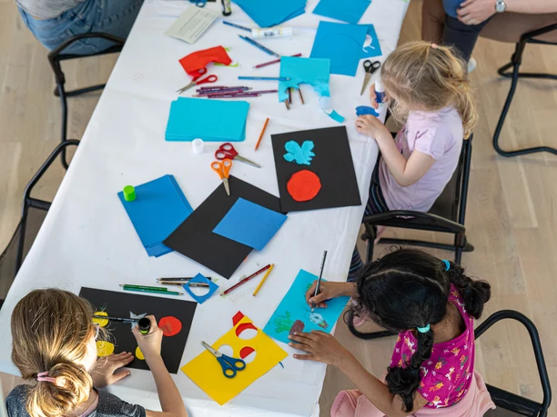 Kunstmuseum Wolfsburg Art4All 04_2025 (c)Marek Kruszewski (12).jpg Kinder und Erwachsene sitzen an einem Tisch. Sie malen und basteln mit buntem Papier.