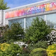 JUB - Junges Theater Bremerhaven_Foto Evelyn Walton_1200x8001692623247.jpg Fassade des Jungen Theaters Bremerhaven mit buntem Banner und blühenden Büschen davor.