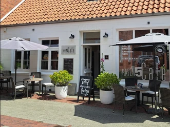 hafen5.png Weißes Café Hafen 5 mit rotem Ziegeldach. Davor stehen Tische, Stühle und Schirme.