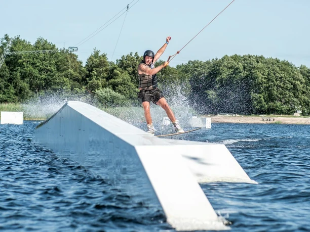 P1500546_Blue Bay Spadener See_Hergen Hanke.jpg Ein Wakeboarder fährt über eine Rampe auf dem Spadener See und lässt das Wasser spritzen.