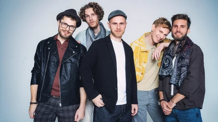 Fünf Musiker der A-cappella-Band Anders posieren vor hellem Hintergrund.