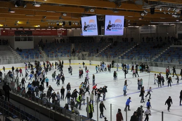 (c)Stadthalle_Bremerhaven__5865 Eisarena Eislauf.JPG Viele Menschen laufen Schlittschuh auf einer großen Eisfläche in einer beleuchteten Halle.