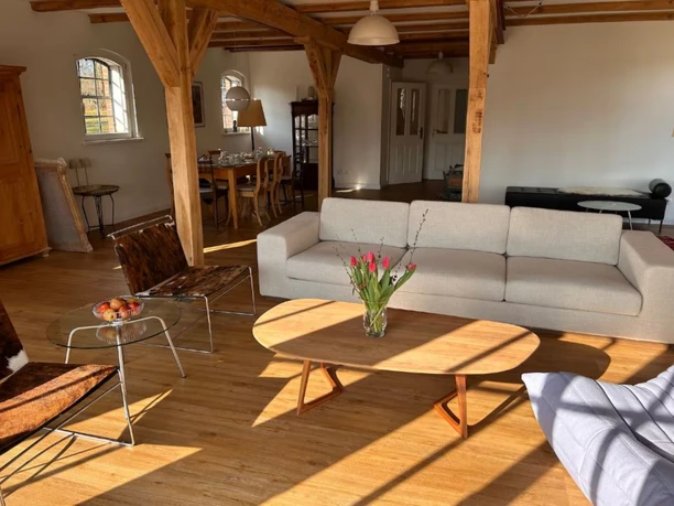 offener-wohn-essbereich-fachwerkhaus Ein weitläufiger Wohnbereich mit Parkettboden, modernem Couchtisch und einem Esstisch im Hintergrund zwischen Holzbalken.