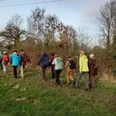 Sportliche Wanderung durch die Sandberge Gruppe von Wandernden mit Rucksäcken auf einem Feldweg. Entlang des Weges stehen Bäume und Sträucher.