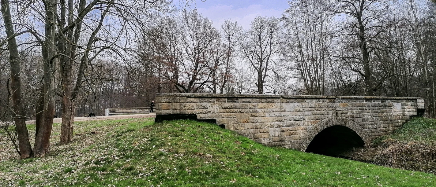 Brücke Hasselbachtal 2.jpg Historische Steinbogenbrücke im Hasselbachtal, umgeben von Bäumen und Rasenflächen.