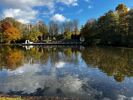 Auf den Spuren von Wassermann, Pau und Kaiser-Friedrich-Park 2 (c) Ökologie-Zentrum Aachen e.V..jpg Umgeben von herbstlichen Bäumen spiegelt sich der blaue Himmel auf der Wasseroberfläche eines Sees.