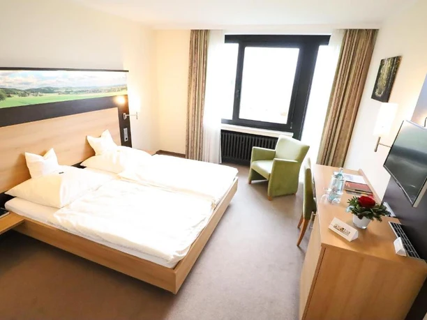 Wiehen-Therme Helles Hotelzimmer mit Doppelbett, Schreibtisch, Sessel und großem Fenster