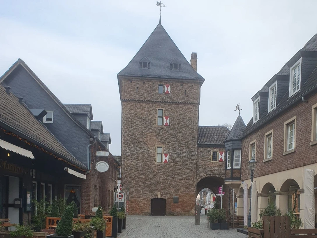 Die Altstadt von Monheim mit interessanten Geschichten von damals und heute Der Schelmenturm in Monheim am Rhein, ein historischer Backsteinturm mit Spitzdach und Torbogen, umgeben von Altstadthäusern.