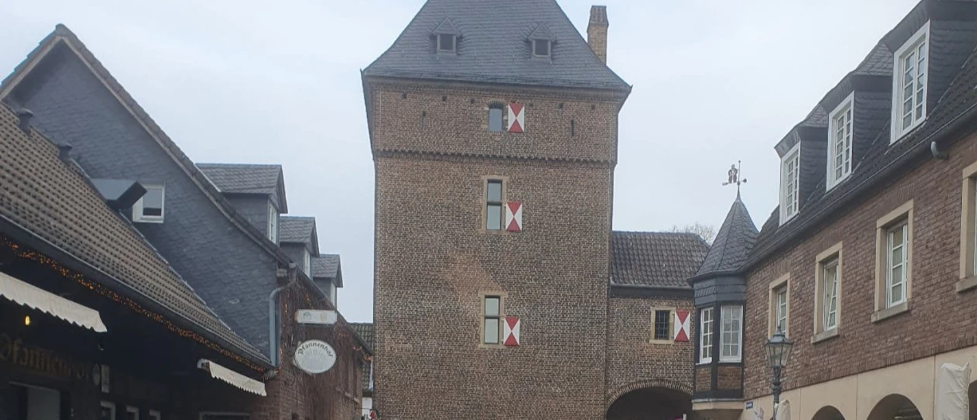 Die Altstadt von Monheim mit interessanten Geschichten von damals und heute Der Schelmenturm in Monheim am Rhein, ein historischer Backsteinturm mit Spitzdach und Torbogen, umgeben von Altstadthäusern.