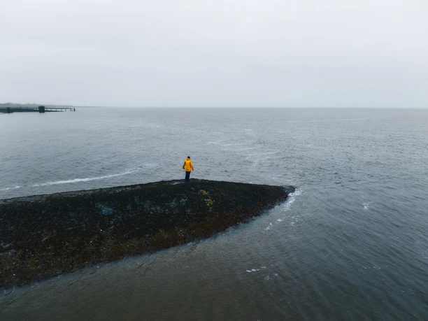 Butjadingen_Wintershooting_Drohne_089.jpg Person in gelber Jacke steht auf einer Buhnenspitze und blickt auf die weite Nordsee.