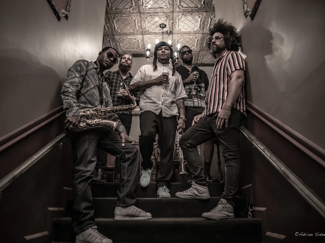 Butter-Funk-Family Fünf Musiker mit Saxofon und Trompete stehen auf einer Treppe im Konzertambiente.