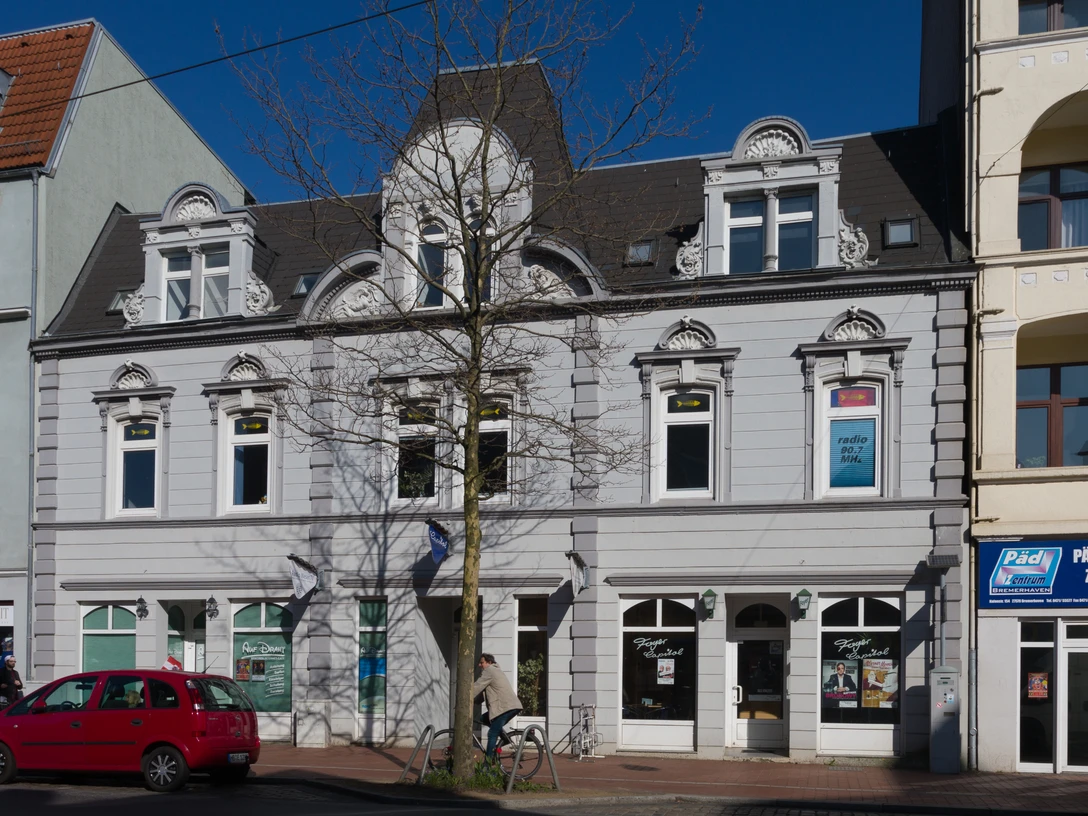 Capitol L1345 (c) Helmut Gross_Erlebnis Bremerhaven.jpg Graue Fassade des historischen Capitol-Gebäudes in Bremerhaven mit Verzierungen und Baum davor.
