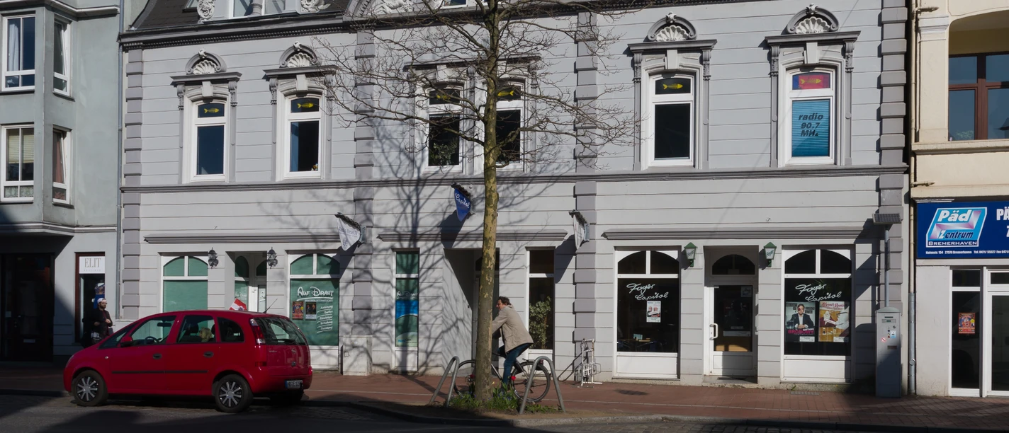 Capitol L1345 (c) Helmut Gross_Erlebnis Bremerhaven.jpg Graue Fassade des historischen Capitol-Gebäudes in Bremerhaven mit Verzierungen und Baum davor.