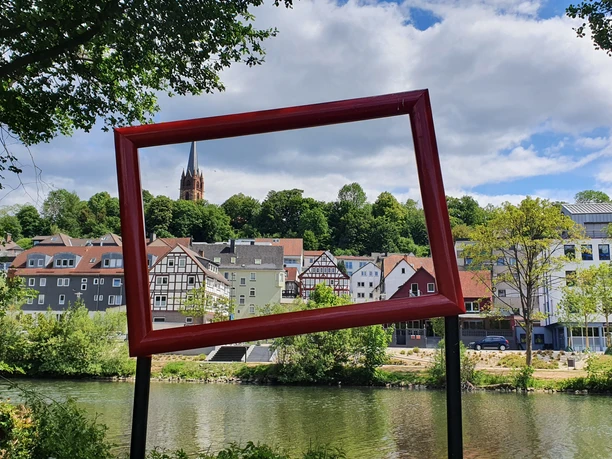 Die Eder an der Uferstraße Frankenberg (Eder) Sie sehen durch einen Bilderrahmen, welcher am Ederufer steht, die Uferstraße von Frankenberg. Im Hintergrund ist der Kirchturm zusehen.