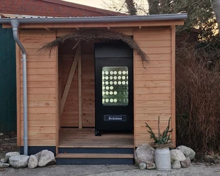 24/7 Eisautomat Schwarzer Eisautomat für Becher-Eis in einer kleinen Holzhütte mit Dekoration.