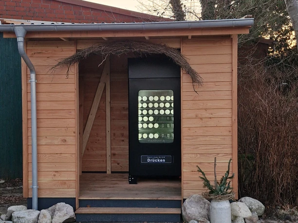 24/7 Eisautomat Schwarzer Eisautomat für Becher-Eis in einer kleinen Holzhütte mit Dekoration.