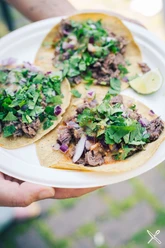Drei frisch belegte Tacos mit Fleisch, Kräutern, Zwiebeln und Limette auf einem Teller.