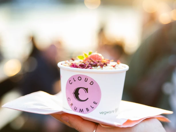 Street Food Festival in Ehrenfeld Hand holding dessert cup with colorful topping in front of blurred background in warm sunlight