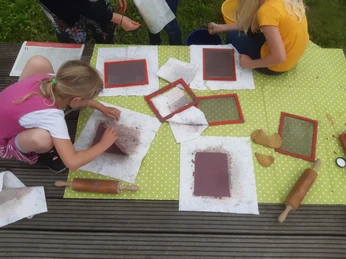 Auf Leppels Spuren Kinder stellen im Freien Papier her, auf einer grünen Decke mit Rahmen und Rollen.