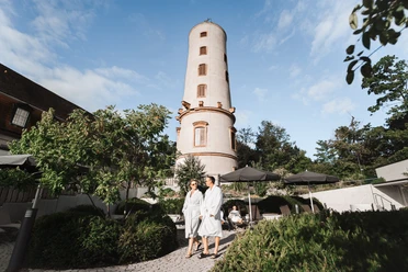 Der Außenbereich mit Blick auf den Sprudelhof Zwei Personen laufen im Bademantel durch den Außenbereich der Sprudelhof Therme