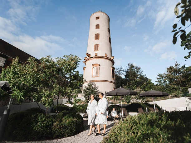 Der Außenbereich mit Blick auf den Sprudelhof Zwei Personen laufen im Bademantel durch den Außenbereich der Sprudelhof Therme