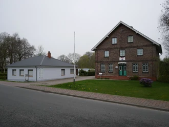 Heimatmuseum Geversdorf Historisches Backsteingebäude neben flachem Anbau des Heimatmuseums Geversdorf an einer Straße.