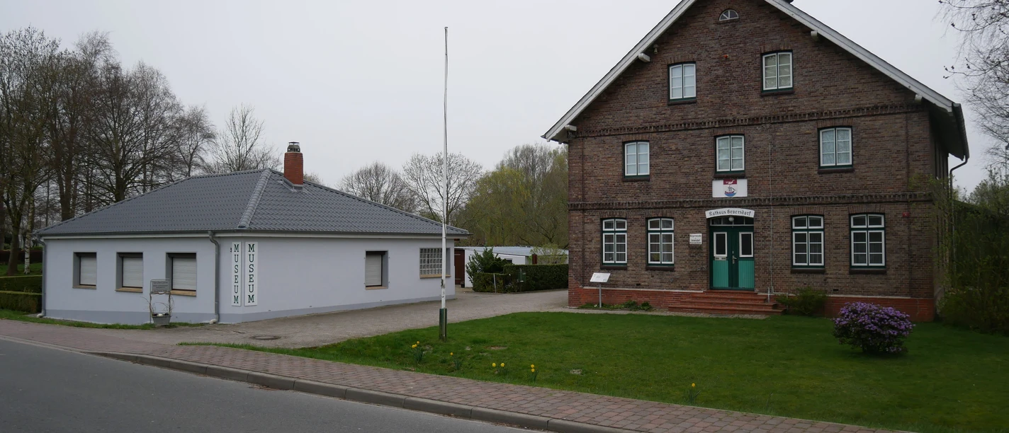 Heimatmuseum Geversdorf Historisches Backsteingebäude neben flachem Anbau des Heimatmuseums Geversdorf an einer Straße.
