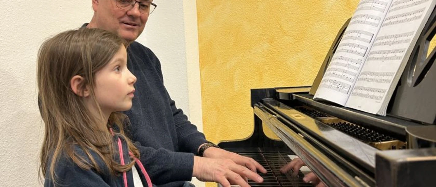 Pro Musica Mädchen spielt Klavier, Lehrer unterstützt beim Schnupperunterricht in der Musikschule